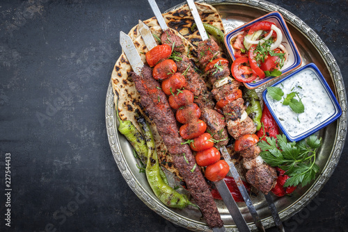 Traditional oriental Adana kebap and shashlik skewer with tomato and flatbread as top view on a plate with copy space left