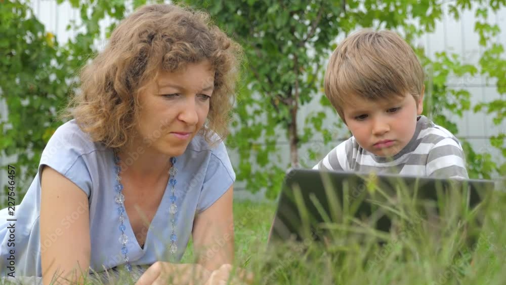 Boy with teacher background. Mother and child. lying on grass. Alternative education. Alternative schooling. Studying outdoors. Home schooling. Teacher and pupil. Outdoor activities. Boy with teacher background. Mother and child. lying on grass. Alternative education. Alternative schooling. Studying outdoors. Home schooling. Teacher and pupil. Outdoor activities.