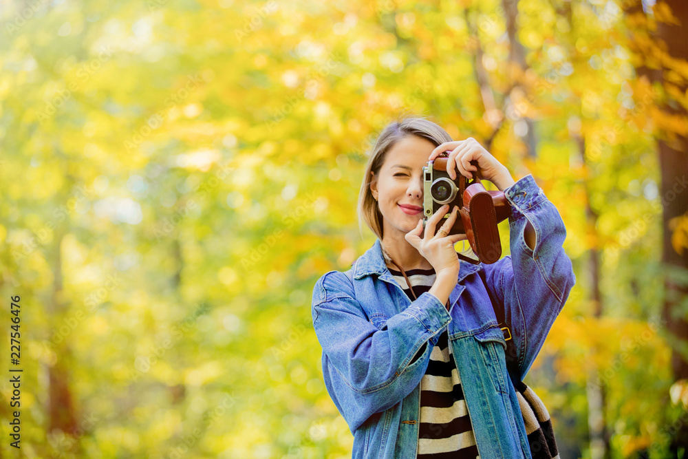 Young beautiful blonde girl with vintage camera have rest in the park in autumn season time.