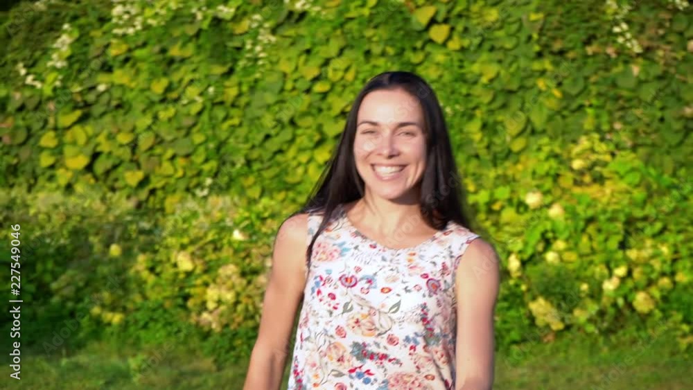European young woman with long black hair runs away from the camera in slow motion, calling for herself. Attractive girl with dimpled cheeks in a white floral print beckons to follow her. Smiling European young woman with long black hair runs away from the camera in slow motion, calling for herself. Attractive girl with dimpled cheeks in a white floral print beckons to follow her. Smiling