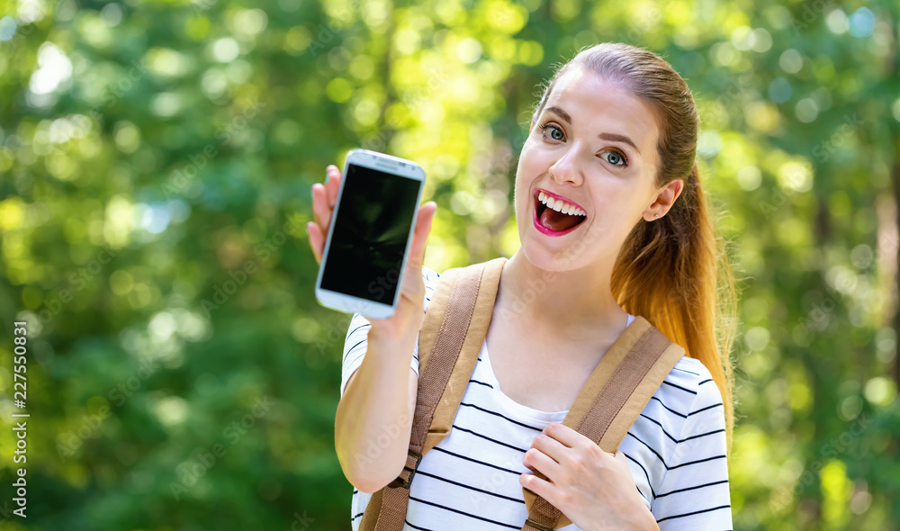 Young woman holding out a smartphone on a bright summer day in the forest