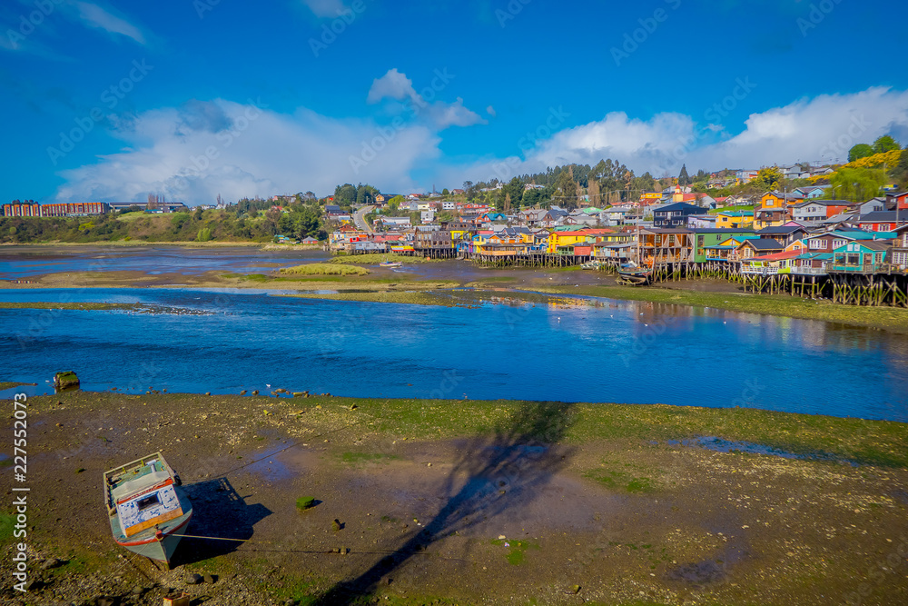 Boat in a low tide with houses on stilts palafitos in the horizont in Castro, Chiloe Island, Patagonia