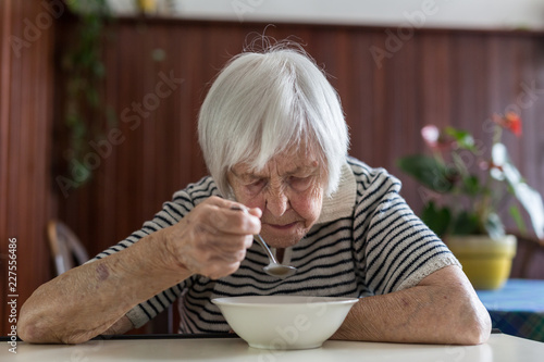 Solitary senior woman eating her lunch at retirement home. Social aid for retirement citizens concept.