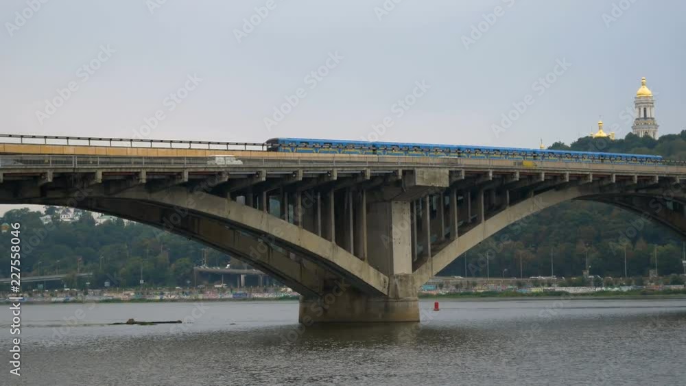 Train travels over the bridge against the sky and the domes of the church. City subway left outside. Public transport on the move. Cars go over the bridge over the river. Train travels over the bridge against the sky and the domes of the church. City subway left outside. Public transport on the move. Cars go over the bridge over the river.