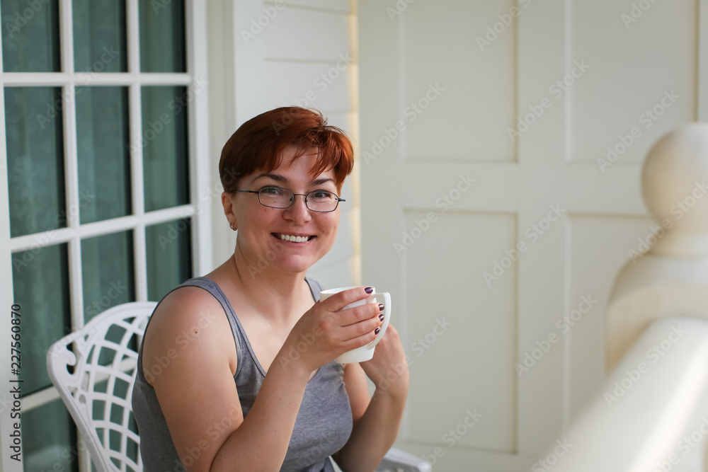 Woman relaxing on balcony holding cup of coffee or tea and looking at camera Woman relaxing on balcony holding cup of coffee or tea and looking at camera