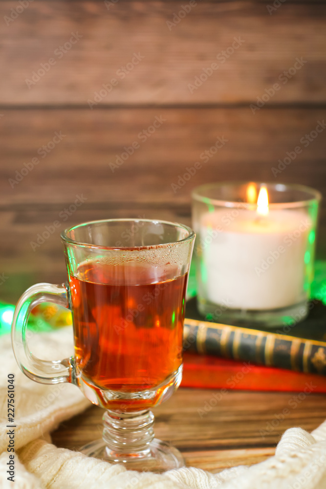 Cozy winter still life: cup of hot tea and books, candle on wooden background and blurred garland lights