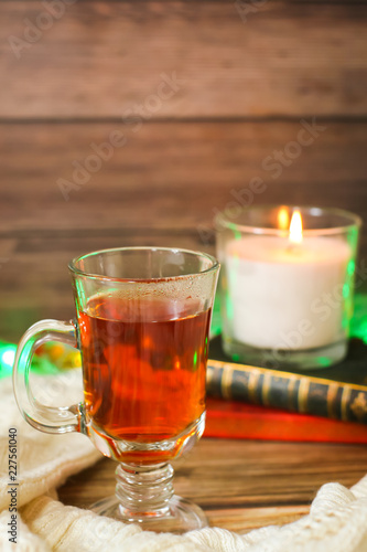 Cozy winter still life: cup of hot tea and books, candle on wooden background and blurred garland lights © Aleksandra