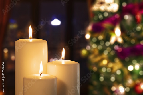 Three white candles with blurred Christmas tree