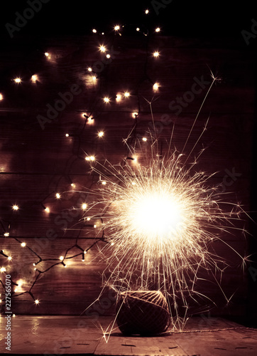 burning sparkler and christmas lights on wooden background