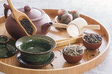 Green tea and tea ceremony attributes - ceramic teapot, cups, strainer, chopsticks and tweezers placed on a wooden tray