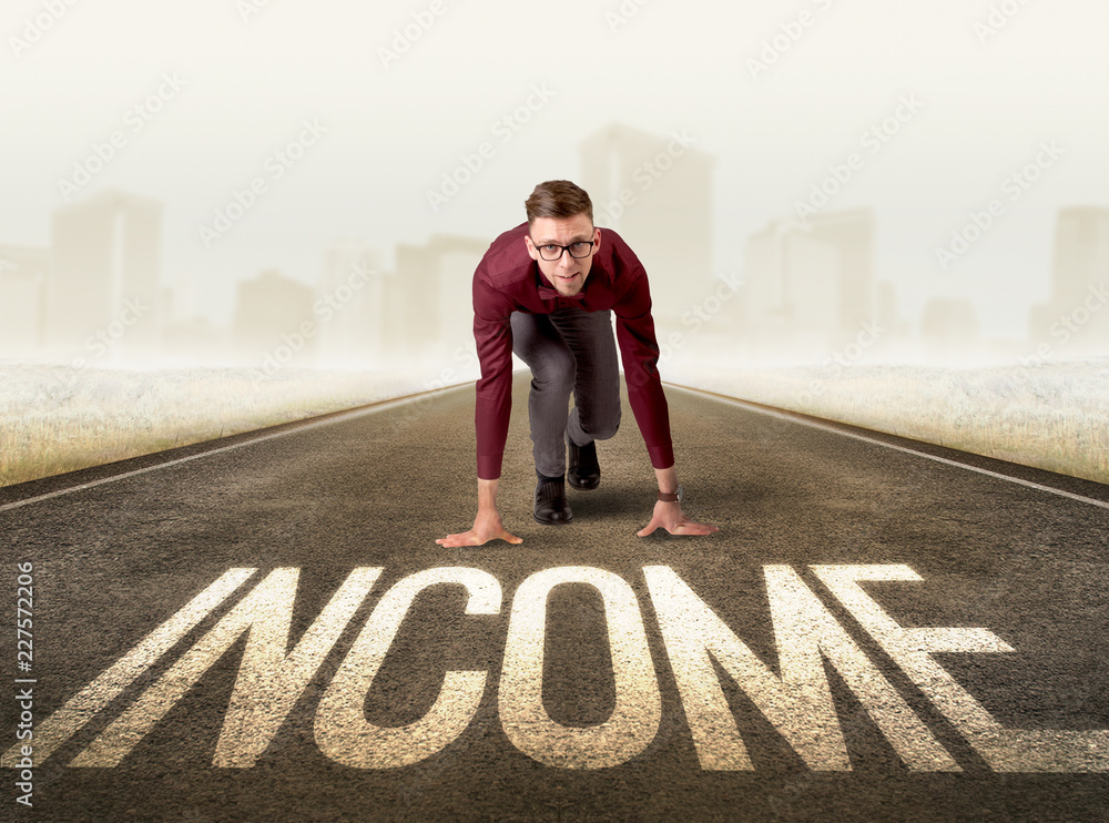 Young determined businessman kneeling before income sign Young determined businessman kneeling before income sign