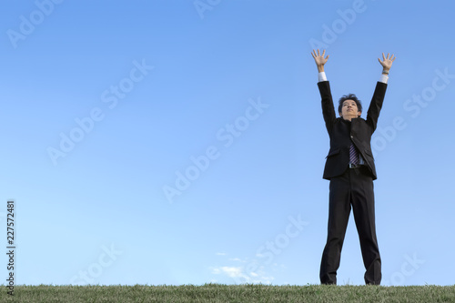 青空をバックに空に向かい手を広げる若い男性1人。成功・勝者・パワー・挑戦イメージ