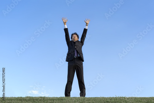 青空をバックに空に向かい手を広げる若い男性1人。成功・勝者・パワー・挑戦イメージ