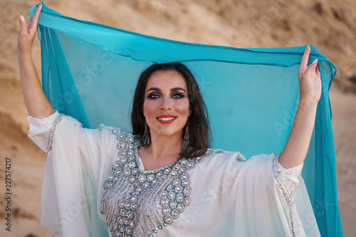 Eastern beauty in suit for performance of national dance Khaleeji. Chaste Oriental dance. Girl in background of golden sands of desert. Houri and heavenly delight. photo