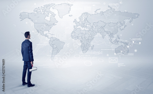 Businessman standing with his back and looking at a worldwide map with objects in his hand 