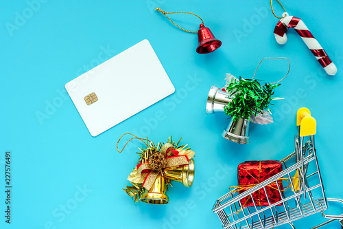 Blank credit chip card with Xmas ornaments and mini shopping cart on blue background for Christmas day and holidays concept photo