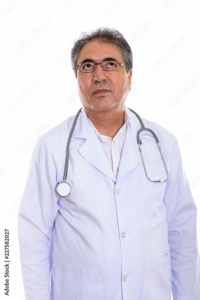Studio shot of senior Persian man doctor thinking while looking Studio shot of senior Persian man doctor thinking while looking