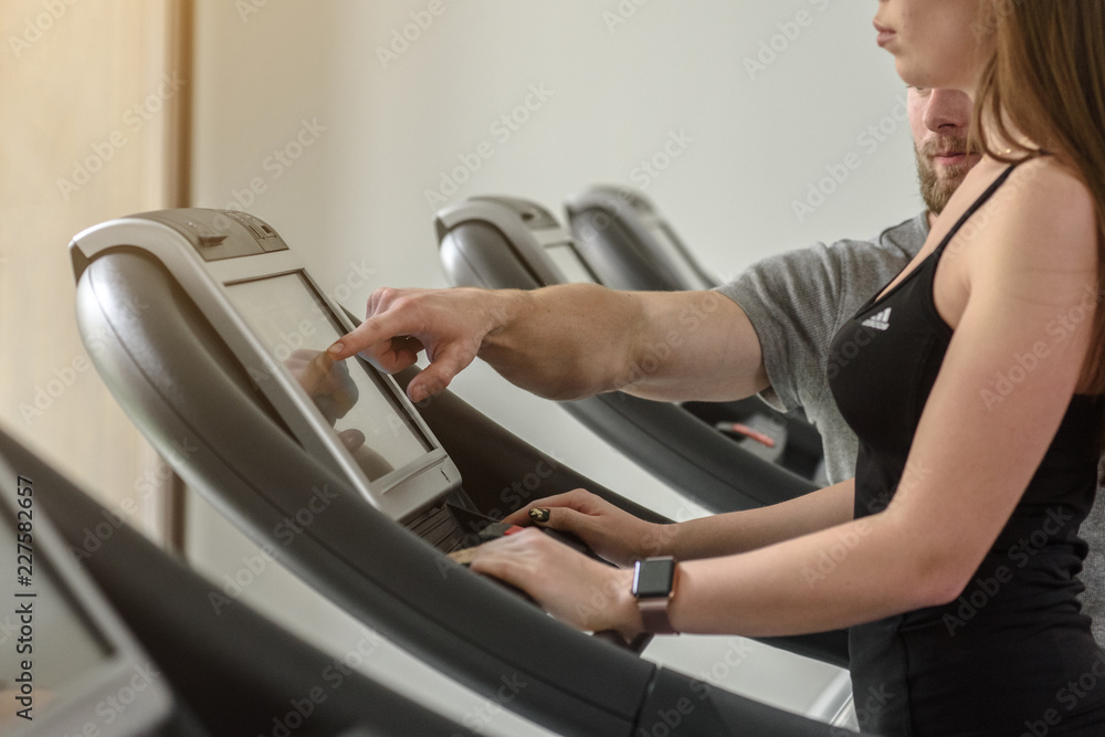 Young woman doing cardio workout on treadmill with personal trainer