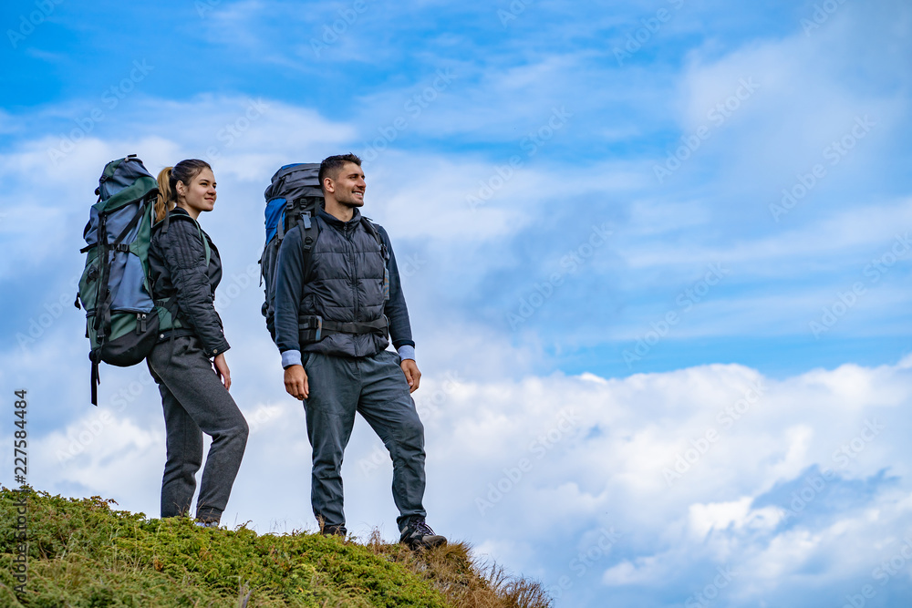 The man and a woman with backpacks standing on the mountain landscape background The man and a woman with backpacks standing on the mountain landscape background
