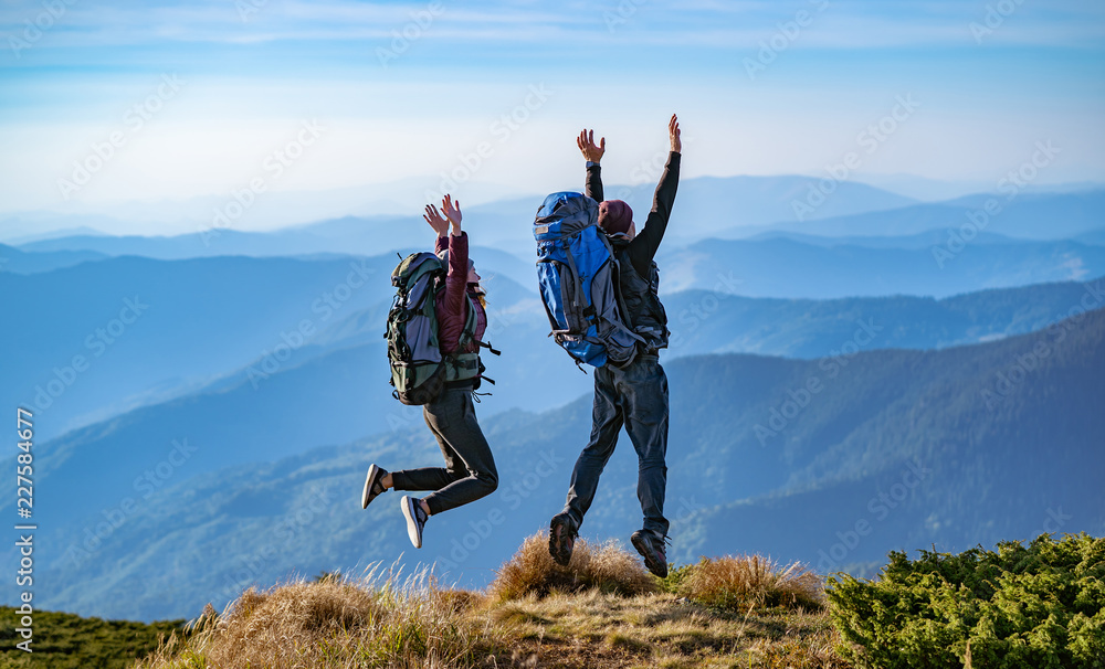 The man and a woman with backpacks jumping on the mountain