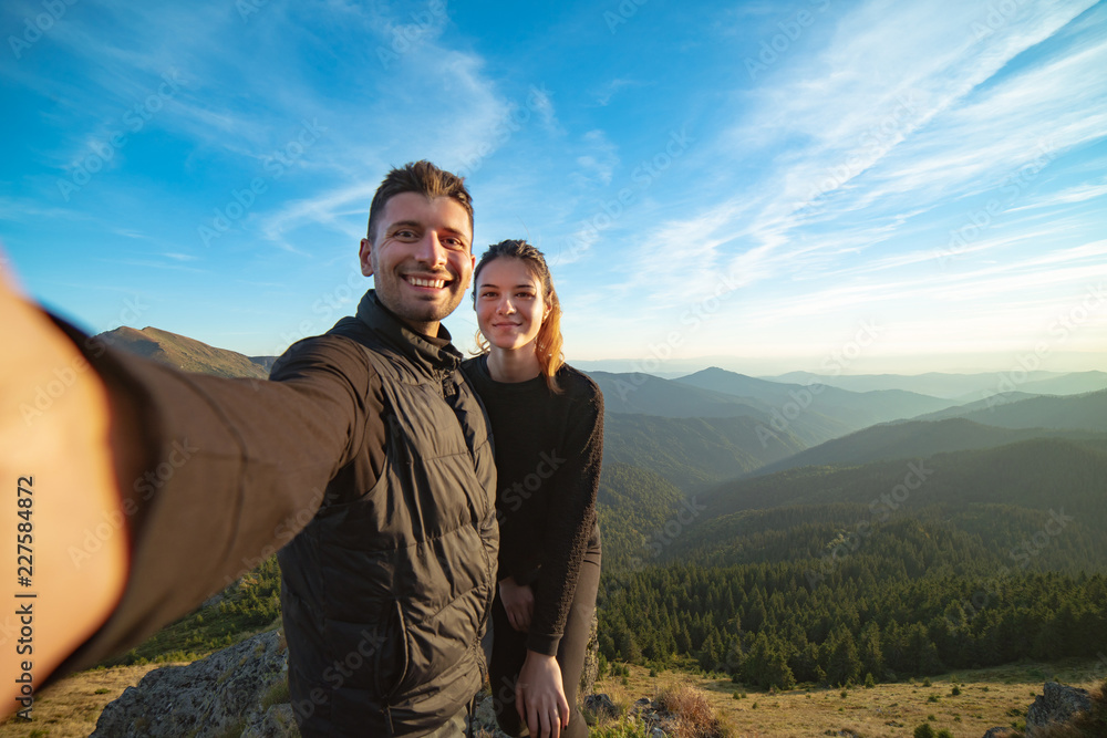 The smiling couple taking a selfie on the mountain background