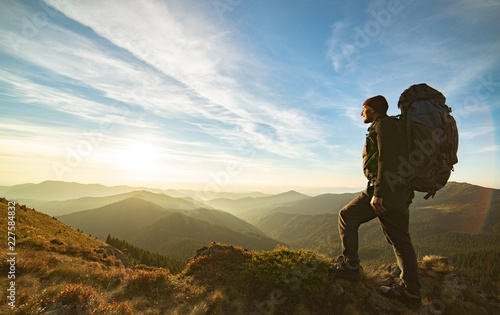 The man standing with a camping backpack on the rock with a picturesque sunrise