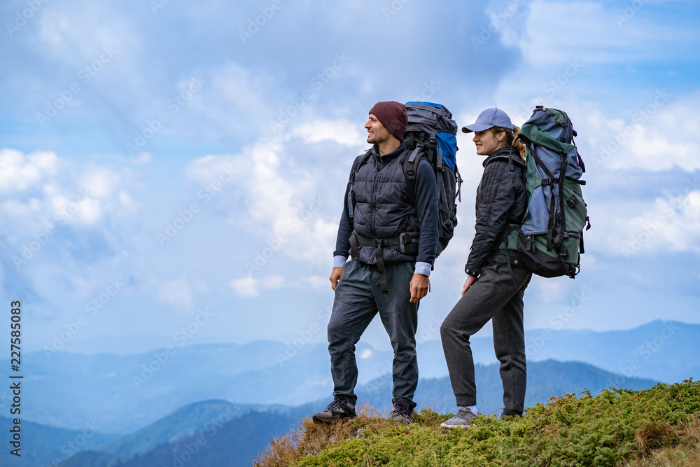 The man and a woman with backpacks standing on the mountain landscape background The man and a woman with backpacks standing on the mountain landscape background