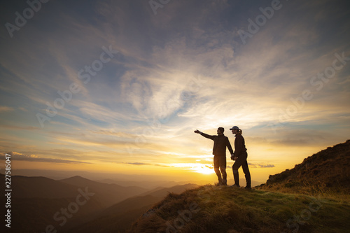 The couple gesturing on the rock with a picturesque sunset