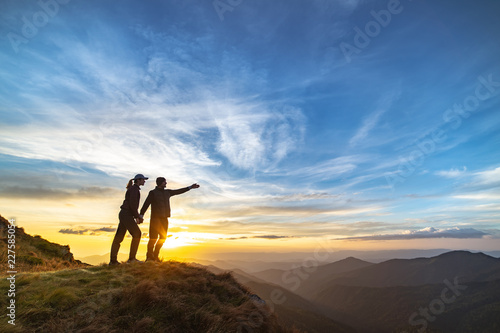 The couple gesturing on the mountain with a picturesque sunset