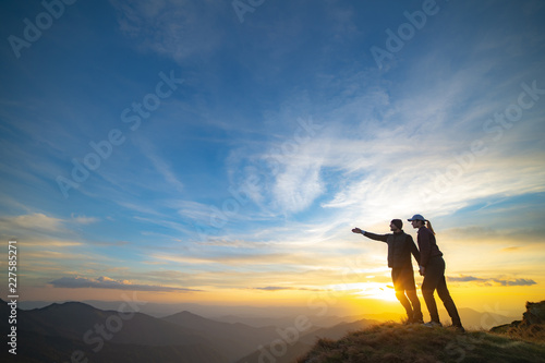 The couple gesturing on the mountain with a picturesque sunset background