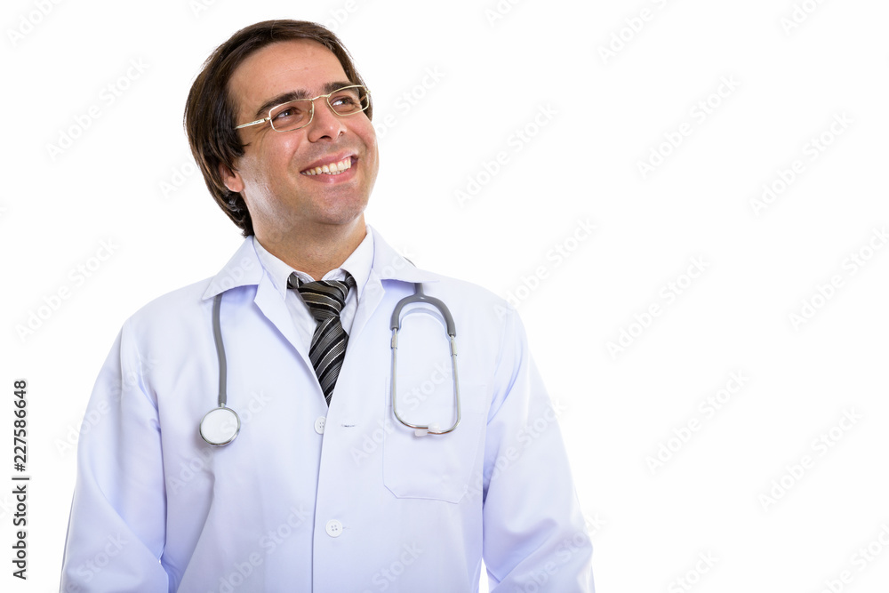 Studio shot of young happy Persian man doctor smiling while thin Studio shot of young happy Persian man doctor smiling while thin