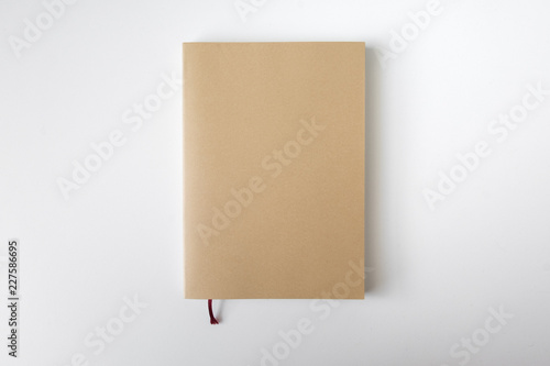 Top view of closed blank craft paper cover notebook with pencil on white desk background