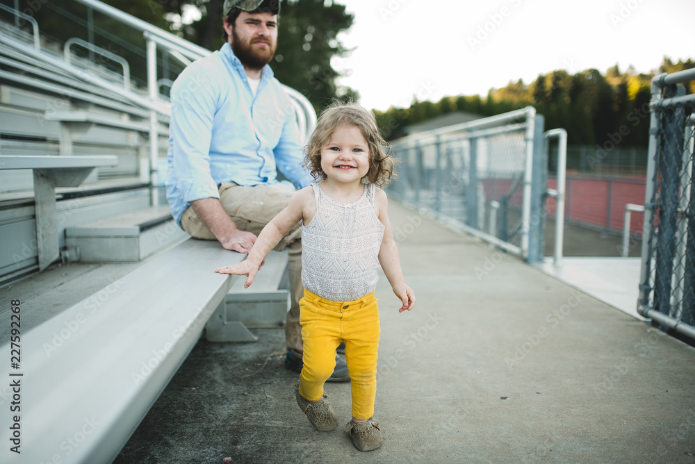 Toddler girl walking away from dad at a football game Toddler girl walking away from dad at a football game