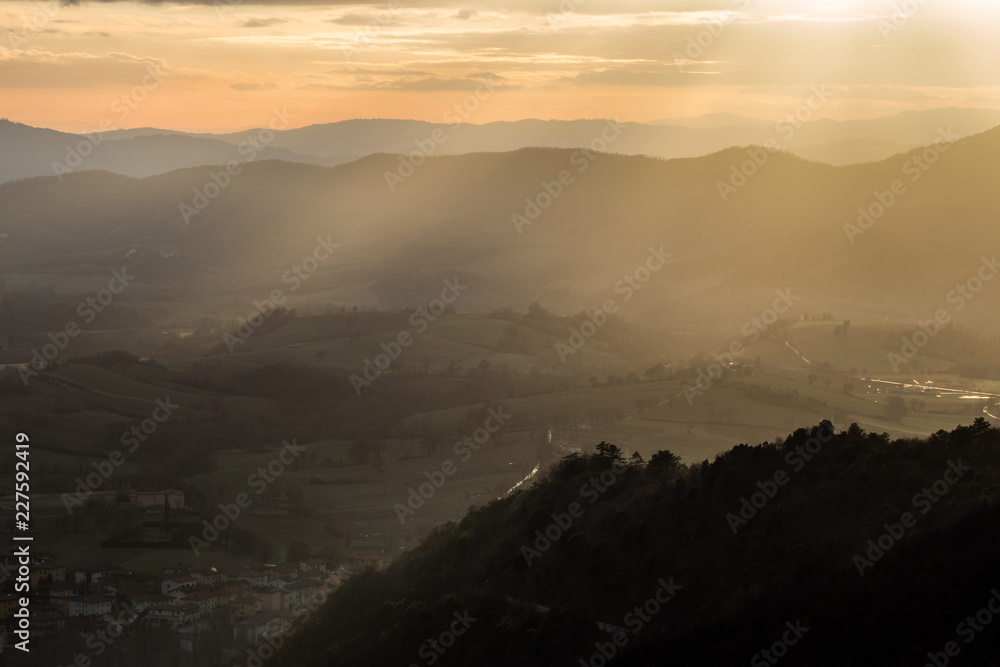Sunrays coming over a valley in Umbria (Italy) with some plants on a hill in the foreground Sunrays coming over a valley in Umbria (Italy) with some plants on a hill in the foreground