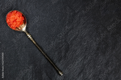 Red fish roe in a spoon, shot from above on a black background with copy space