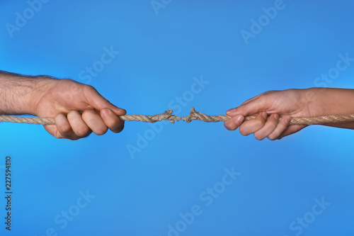 Woman and man pulling damaged rope on color background