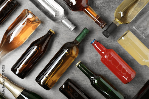Bottles with different alcoholic drinks on grey background, flat lay