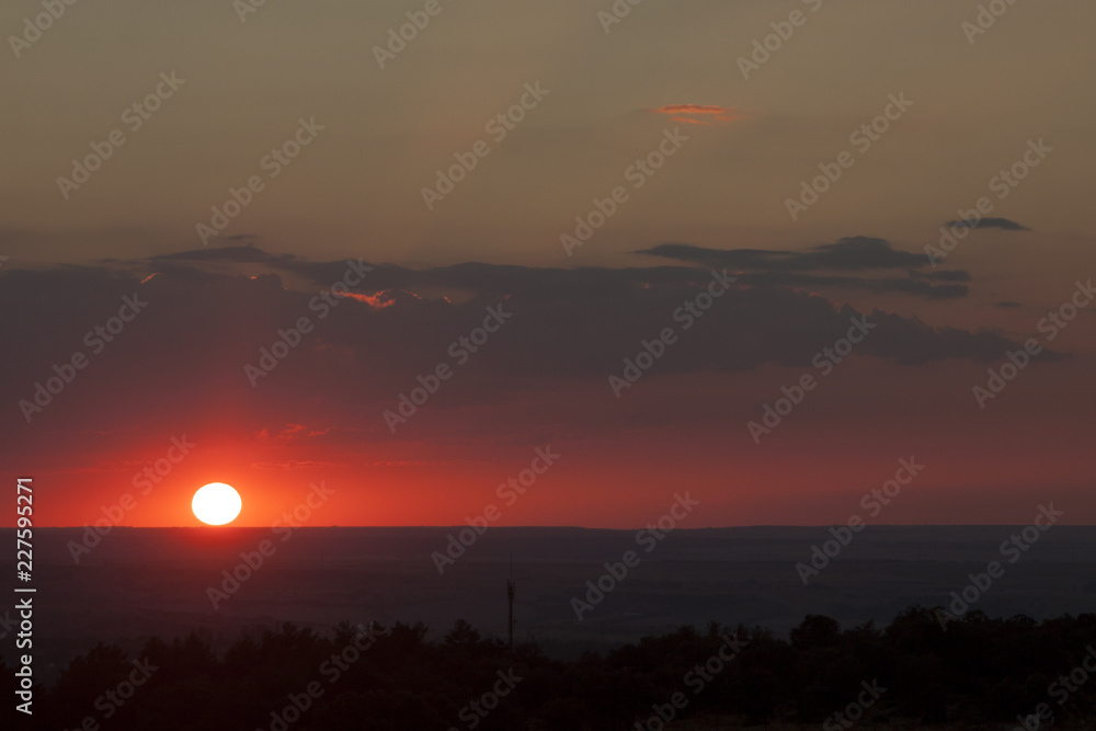 Fototapeta premium Natural sun exposure on field or meadow. Bright dramatic sky and dark earth. Countryside landscape under scenic colorful sky at sunset. Sun over the horizon. Warm colors