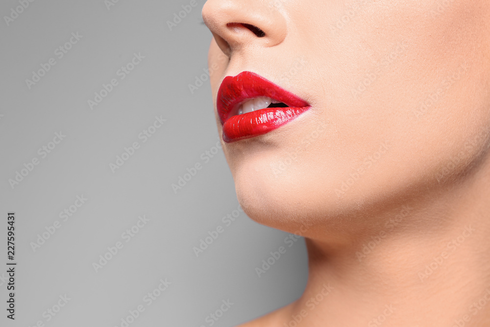 Beautiful young woman with red glossy lips on gray background, closeup. Space for text Beautiful young woman with red glossy lips on gray background, closeup. Space for text