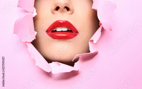 View of beautiful young woman with red lips through hole in color paper, closeup