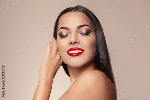 Portrait of beautiful young woman with red glossy lips on color background