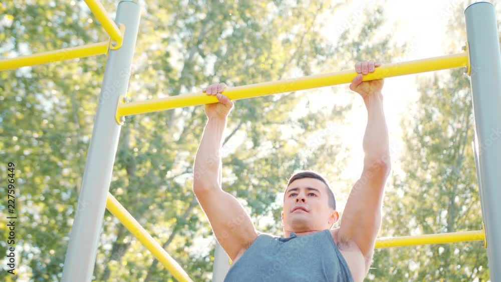 Pull-up strength training exercise. Slim athlete a very fit guy fitness instructor or a personal trainer working out his arm muscles on outdoor beach gym as part of a crossfit workout. Pull-up strength training exercise. Slim athlete a very fit guy fitness instructor or a personal trainer working out his arm muscles on outdoor beach gym as part of a crossfit workout.