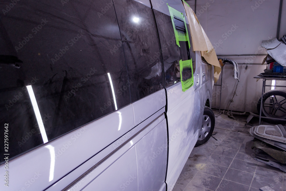Preparing for painting a silver bus in a body repair shop in a separate box service station. Putting putty and leveling the surface of the door before painting.