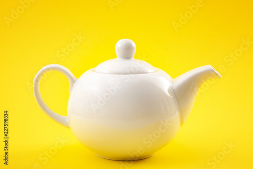 White ceramic teapot, china pot or tea kettle isolated on yellow background