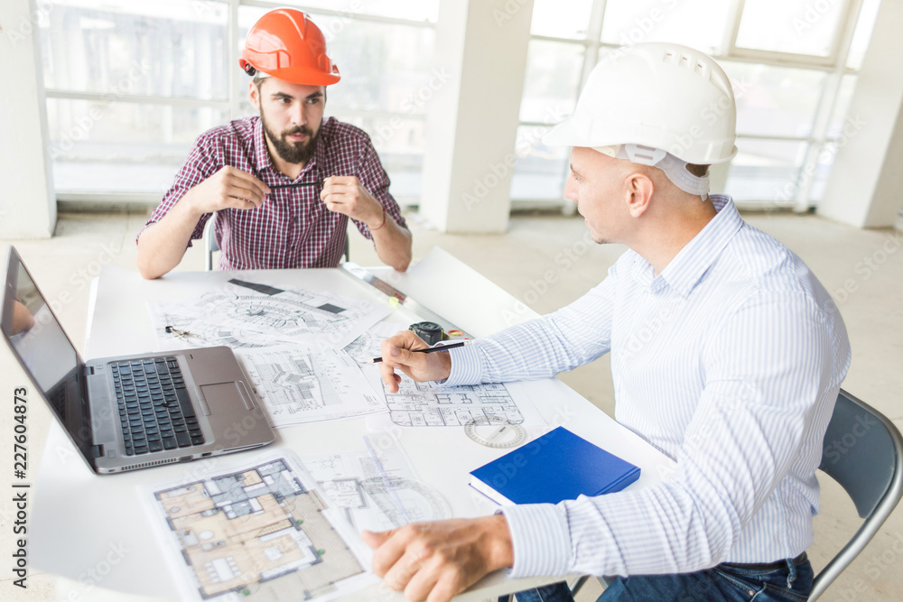 male engineers, architects working at the desk in helmets. Drawings, laptop, roulette on the desktop. Reception and supervision of building construction male engineers, architects working at the desk in helmets. Drawings, laptop, roulette on the desktop. Reception and supervision of building construction
