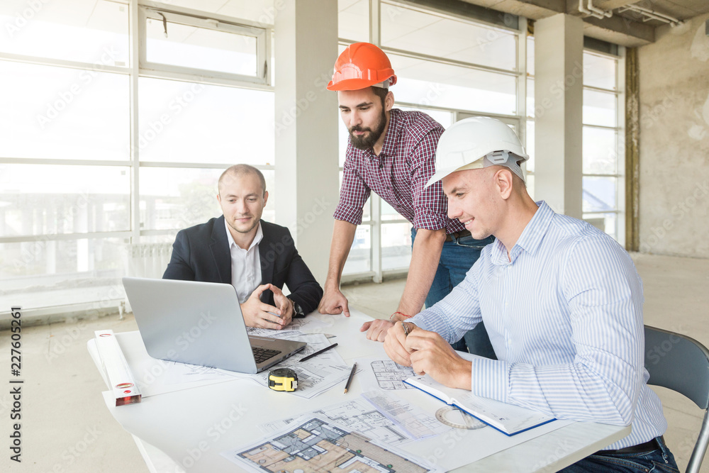 male engineers, architects working at the desk in helmets. Drawings, laptop, roulette on the desktop. Reception and supervision of building construction male engineers, architects working at the desk in helmets. Drawings, laptop, roulette on the desktop. Reception and supervision of building construction