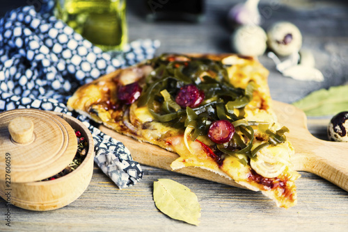 slice of pizza with sausage and seaweed, cheese on a wooden background