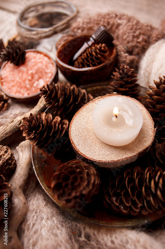 Spa and wellness setting with sea salt, oil essence, cones and candle, wooden decor on wooden background. Fall autumn winter wellness concept, Relax and treatment therapy.