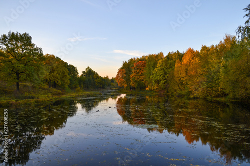 Beautiful autumn landscape. Lake, yellow and red trees by the lake. Reflection in water. Blue sky. Sunny autumn day
