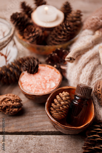 Spa and wellness setting with sea salt, oil essence, cones and candle, wooden decor on wooden background. Fall autumn winter wellness concept, Relax and treatment therapy.